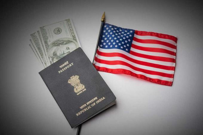 背景にアメリカ国旗が付いたインドのパスポートとアメリカの紙幣またはドルを示し、アメリカ人観光客またはH-1Bビザまたは旅行ビザを申請するコンセプト