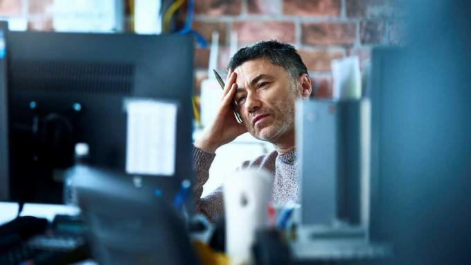 impiegato maschio che guarda lo schermo del suo computer con un'espressione stressata e stanca
