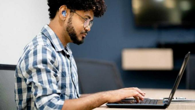 Ein junger Mann mit Hörgerät arbeitet an einem Laptop.
